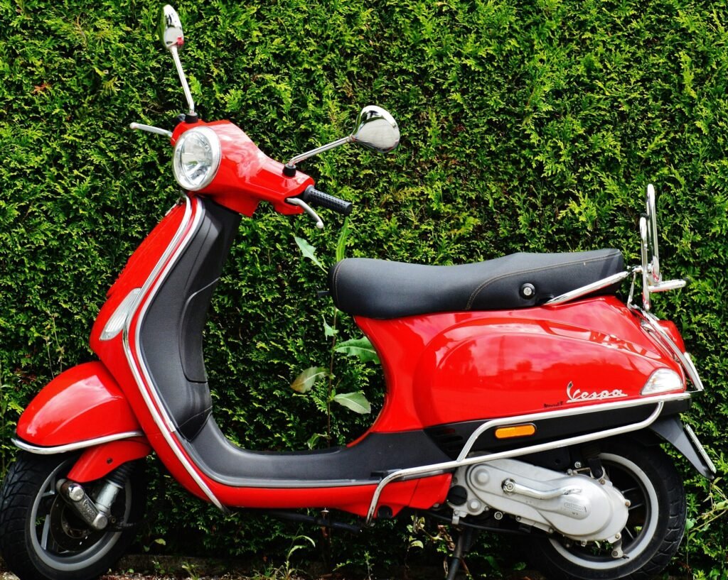 Bright red Vespa scooter parked against a lush green hedge, showcasing vibrant contrast.